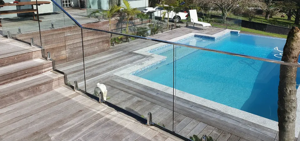 Glass pool fence running beside timber steps and a deck next to a pool