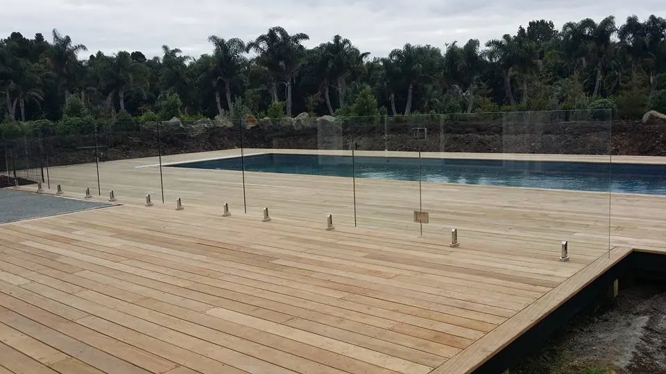 Glass pool fence with spigots along a long timber deck beside a pool