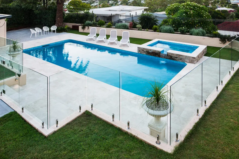 Frameless glass pool fence around a rectangular pool and spa with a pale tiled surround, seen from above