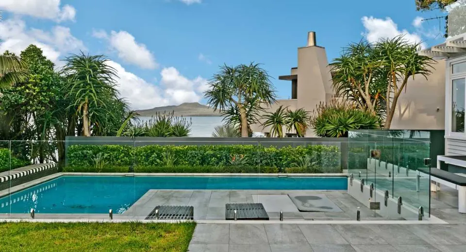 Glass pool fence along a landscaped pool with palm trees behind