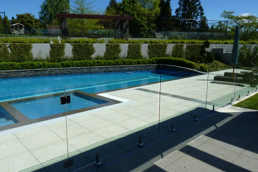 Glass pool fence around a pool corner with pale paving