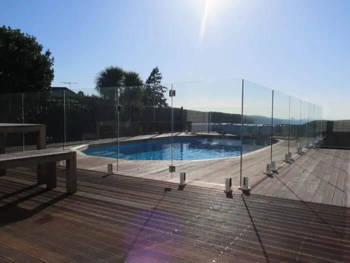 Glass pool fence around a round pool with a timber deck in strong sun