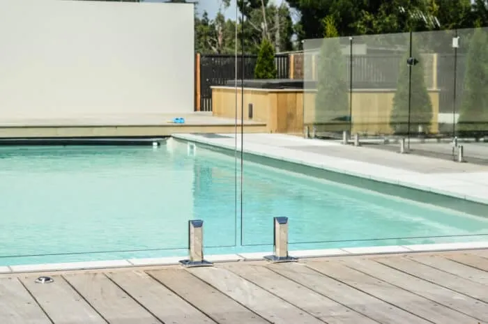 Glass pool fence panels held by stainless spigots on a timber deck beside a pool